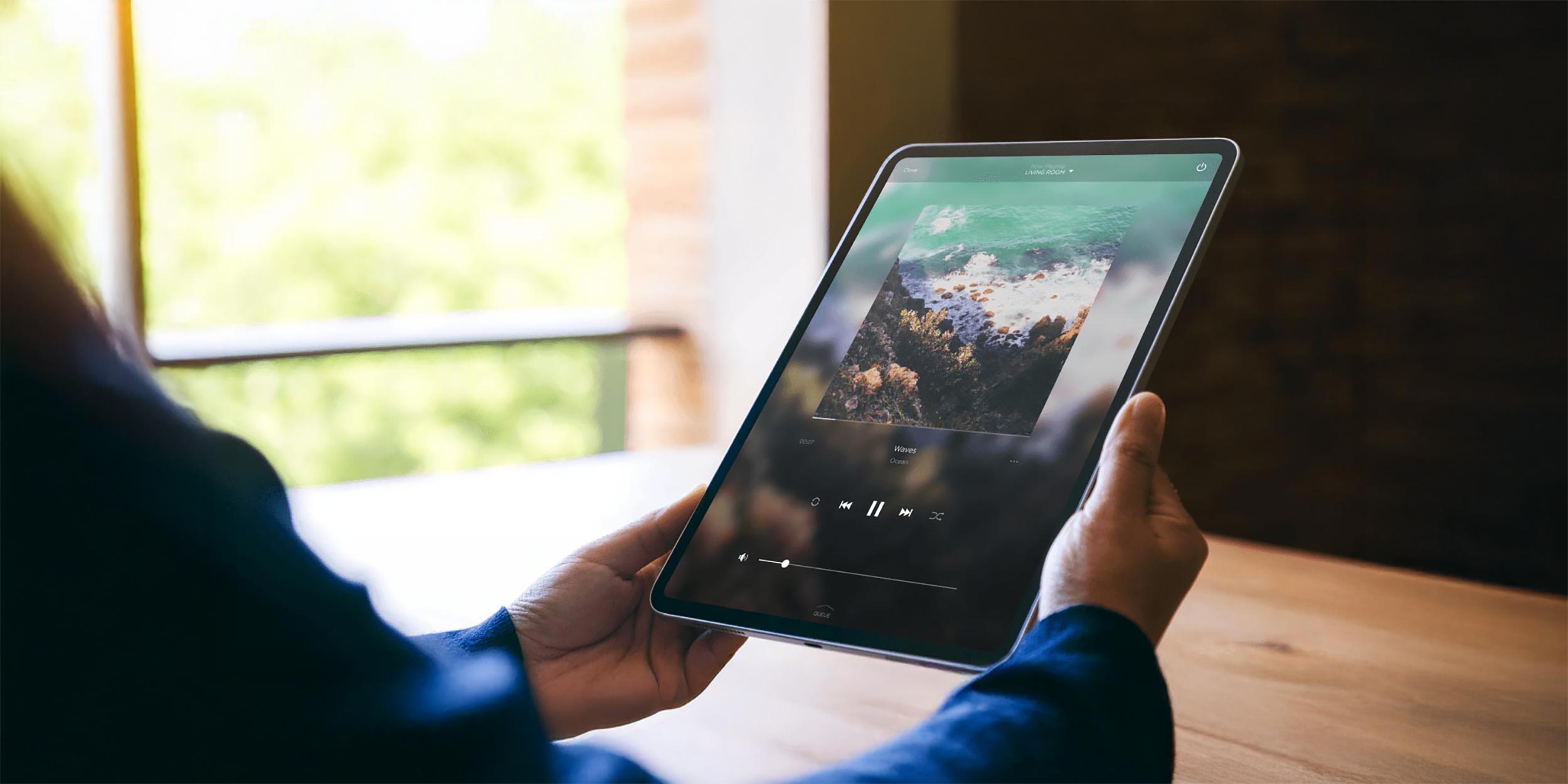 Person holding a tablet playing music with album art displayed on screen