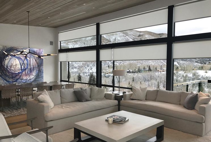 Contemporary living room with white roller shades and mountain scenery visible through large windows