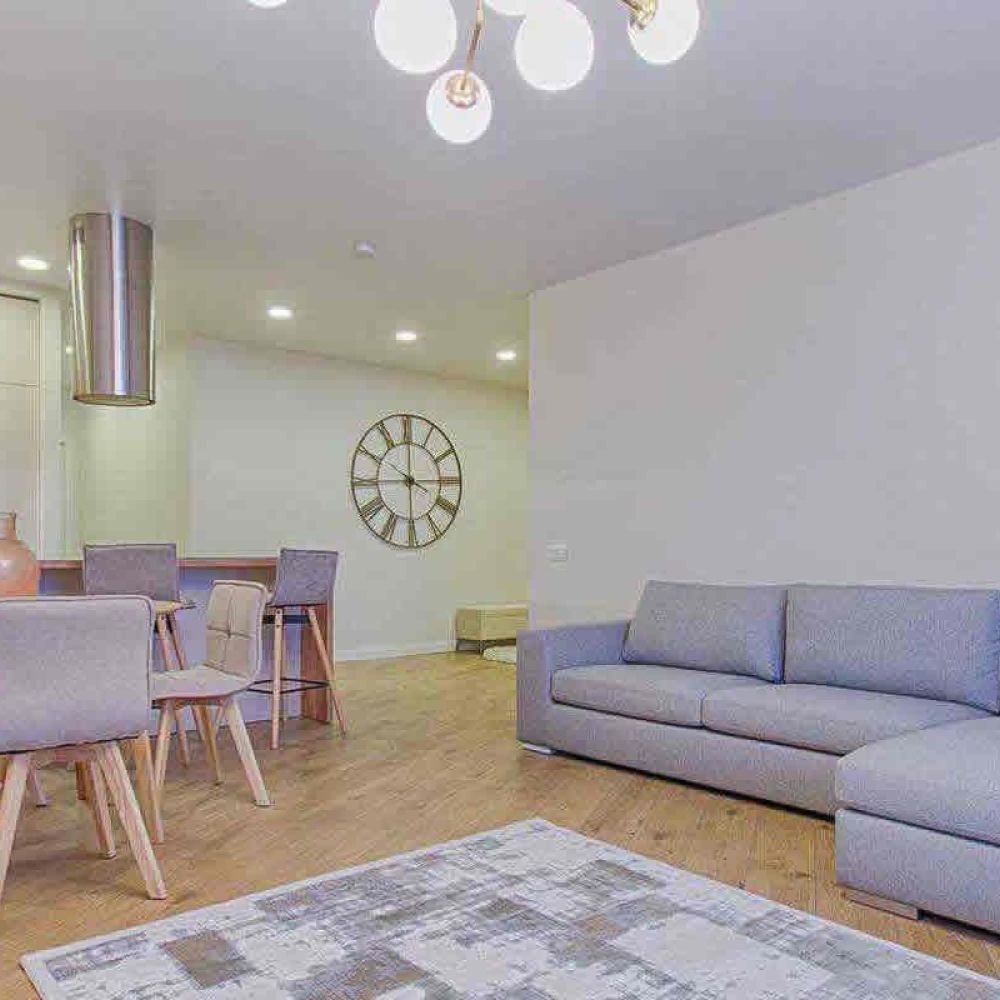 <span class="uk-h4">A modern living room with a gray sectional sofa, a dining area with a round table and chairs, and stylish lighting fixtures, creating a cozy and elegant ambiance.</span>