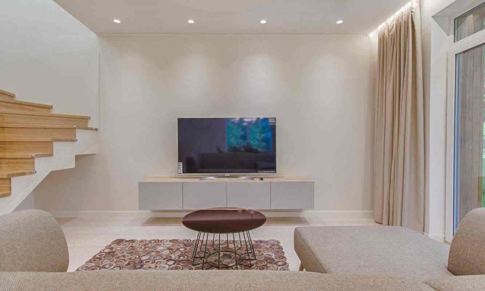 <span class="uk-h4">A modern living area with a beige sectional sofa, a flat-screen TV, a wooden staircase, and large windows, offering a bright and open design.</span>